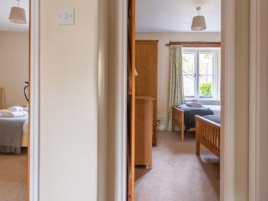 A view through a doorway into two bedrooms each with wooden beds and folded towels at Bassicks in Hawkshead