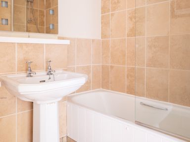 A bathroom with a white pedestal sink and a bathtub with beige tiled walls at Bassicks Hawkshead