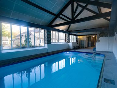 An indoor swimming pool with large windows and exposed beams at Hilltop in Graythwaite near Hawkshead