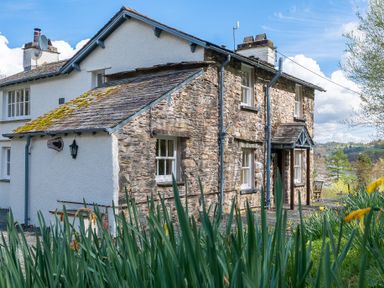 A stone and white plaster house with windows and a small porch surrounded by plants at Hilltop in Graythwaite near Hawkshead