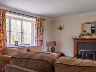 A living room with brown sofas a window with patterned curtains and a fireplace at Hilltop in Graythwaite near Hawkshead