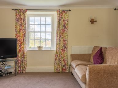 A living room with colorful curtains a television on a stand and a brown sofa with a purple cushion at Hilltop in Graythwaite near Hawkshead