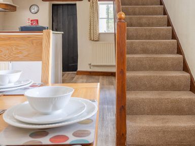 A dining table with white plates and bowls next to a carpeted staircase and a window with curtains at Hilltop in Graythwaite near Hawkshead