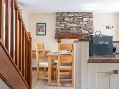 A dining area with wooden chairs and table set with bowls near a stone fireplace and wooden stairs at Hilltop in Graythwaite near Hawkshead