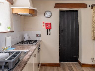 A kitchen counter with a sink a dish rack a gas stove a kettle and a clock above a black door at Hilltop in Graythwaite near Hawkshead