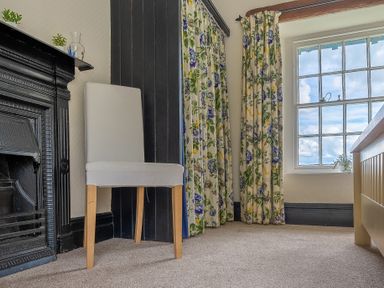 A room corner with a white chair beside a black fireplace and floral curtains near a window at Hilltop in Graythwaite near Hawkshead