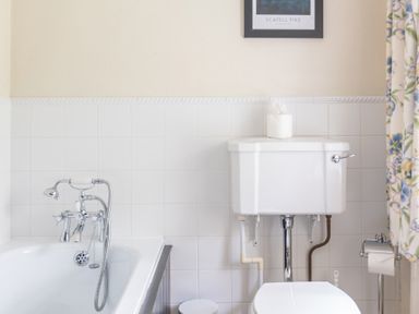 A bathroom with a white bathtub with a shower attachment and a toilet with a tissue box on the tank at Hilltop in Graythwaite near Hawkshead