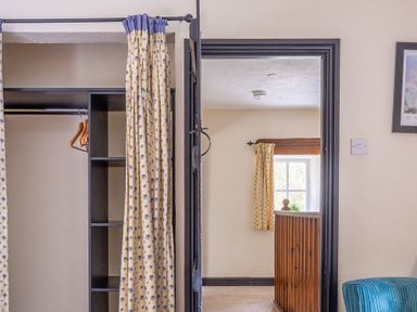An open wardrobe with a curtain and hangers next to a doorway showing a window and wooden railing at Hilltop in Graythwaite near Hawkshead