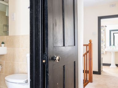 A bathroom with a white toilet and sink visible through a black door in a hallway with carpet and a wooden stair railing at Hilltop in Graythwaite near Hawkshead