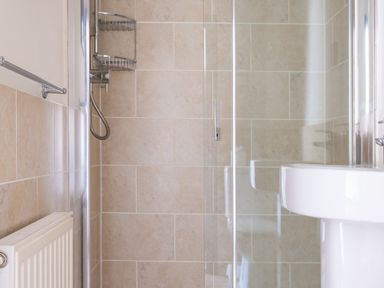 A shower area with beige tiled walls a glass door a white sink and a radiator in a bathroom at Hilltop in Graythwaite near Hawkshead