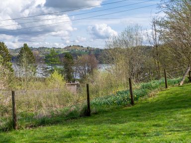 A grassy garden area with a wire fence and trees overlooking a body of water and hills at Hilltop in Graythwaite near Hawkshead