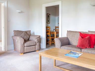 A living room with a brown armchair and sofa with red cushions and a wooden coffee table with a magazine at Mill Cottage in Graythwaite near Hawkshead