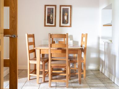 A dining area with a wooden table and five wooden chairs on tiled floor with two framed pictures on the wall at Mill Cottage in Graythwaite near Hawkshead