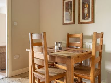 A dining area with a wooden table and four wooden chairs with placemats and salt and pepper shakers on the table at Mill Cottage in Graythwaite near Hawkshead
