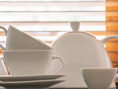 White teapot with stacked teacups and saucers on a table in front of wooden blinds at Mill Cottage in Graythwaite near Hawkshead