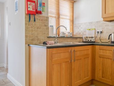 A kitchen corner with wooden cabinets a sink a toaster kettle and a fire blanket on the wall at Mill Cottage in Graythwaite near Hawkshead