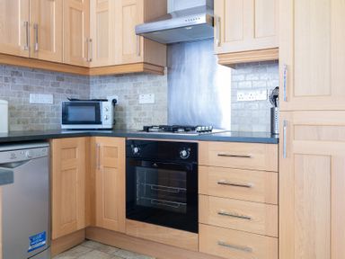 A kitchen with wooden cabinets a microwave oven a gas stove a black oven and a dishwasher at Mill Cottage in Graythwaite near Hawkshead