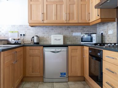 A kitchen with wooden cabinets a dishwasher toaster kettle microwave and oven at Mill Cottage in Graythwaite near Hawkshead