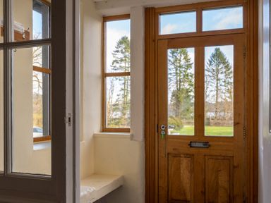 An entryway with a wooden door and side windows showing trees outside at Mill Cottage Graythwaite near Hawkshead
