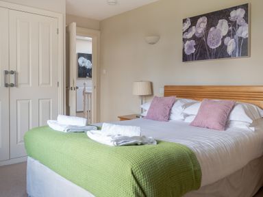 A bedroom with a double bed covered with a green blanket and two pink cushions at Mill Cottage in Graythwaite near Hawkshead