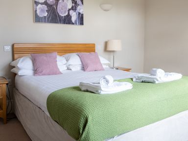 A bedroom with a double bed green blanket purple cushions and rolled towels at Mill Cottage in Graythwaite near Hawkshead