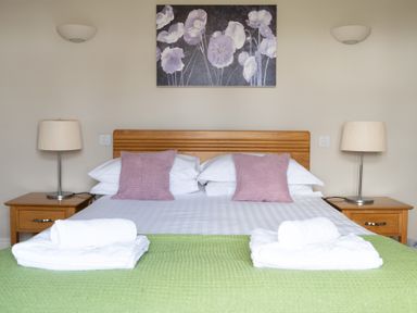 A bedroom with a double bed with purple cushions and green blanket with bedside tables and lamps at Mill Cottage in Graythwaite near Hawkshead