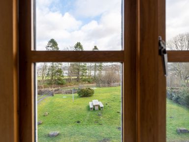 A grassy garden with a picnic table and wooden fences seen through a wooden window frame at Mill Cottage Graythwaite near Hawkshead