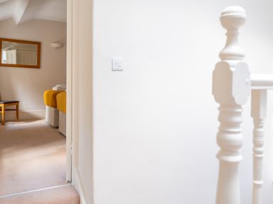 A hallway with a white wooden railing and a view into a room with twin beds covered in yellow blankets and a wooden chair Mill Cottage Graythwaite near Hawkshead