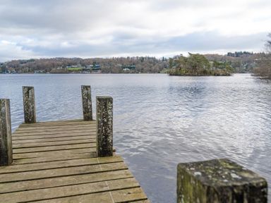 A wooden dock extending into a lake with an island and houses on the far shore at Mill Cottage in Graythwaite near Hawkshead