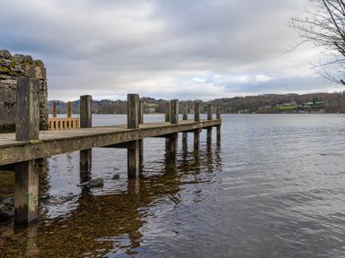 A wooden dock extending into a calm lake with hills and houses in the background at Mill Cottage in Graythwaite near Hawkshead