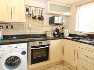 A kitchen with light wood cabinets a washing machine oven stovetop microwave kettle and sink at 2 Lock Cottages in Honing near East Ruston