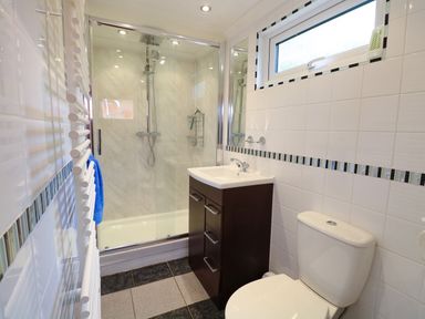 A bathroom with a shower enclosure a sink with cabinet a toilet and a window at 2 Lock Cottages Honing near East Ruston