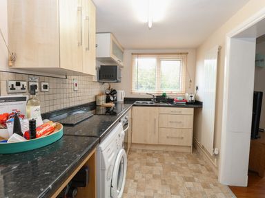 A kitchen with black countertops wooden cabinets a washing machine and a window with blinds at 2 Lock Cottages Honing near East Ruston