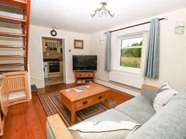 A living room with wooden floor a sofa a coffee table a television and a staircase at 2 Lock Cottages Honing near East Ruston
