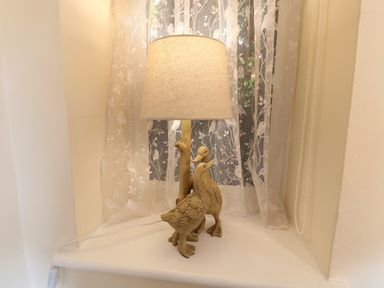 A lamp with a carved wooden base featuring two ducks on a windowsill with lace curtains at 2 Lock Cottages in Honing near East Ruston