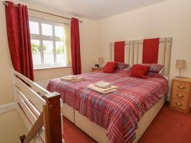 A bedroom with a double bed, bedside tables with lamps, and a window with red curtains at 2 Lock Cottages in Honing near East Ruston