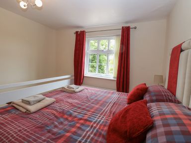 A bedroom with a double bed with checked red and blue bedding and red curtains at 2 Lock Cottages in Honing near East Ruston