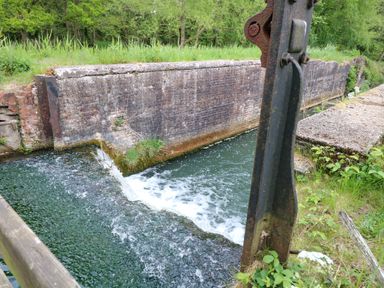 A small canal lock with water flowing over the edge and surrounded by greenery at 2 Lock Cottages Honing near East Ruston