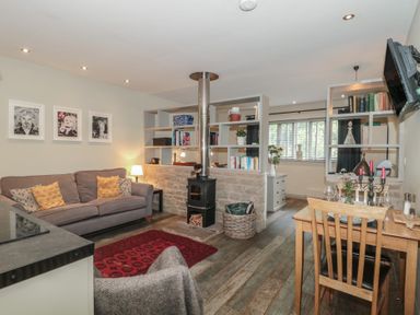 A living room with a sofa, wooden stove, and dining area at The Stable in Deepdean near Ross-on-Wye