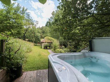 A hot tub overlooking a garden pathway and shelter at The Stable in Deepdean near Ross-on-Wye