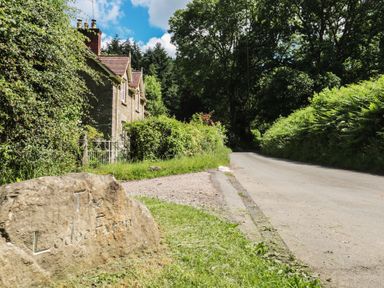A stone sign and house by a road at The Lodge Farm in Deepdean near Ross-on-Wye