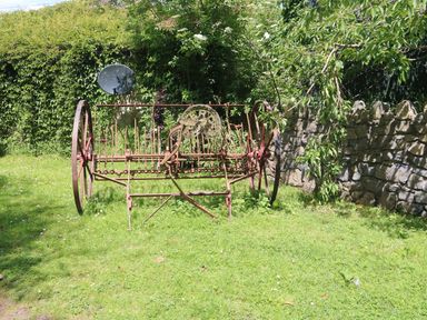 An old rusty farming tool on grass near a stone wall and leafy bushes at Mrs Delaneys Loft in Ardfinnan near Clonmel County Tipperary