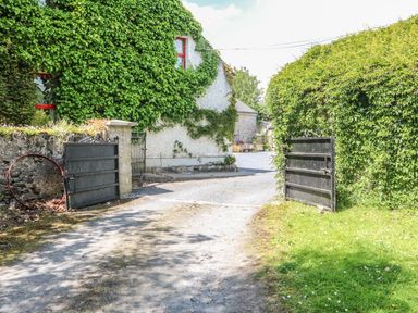A driveway with open black metal gates and a house covered in ivy at Mrs Delaney's Loft in Ardfinnan near Clonmel County Tipperary