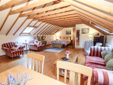 An attic bedroom with exposed wooden beams striped armchairs a bed and a wooden table at Mrs Delaneys Loft Ardfinnan near Clonmel County Tipperary