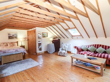 An attic bedroom with wooden beams a bed a sofa armchair and a coffee table at Mrs Delaneys Loft in Ardfinnan near Clonmel County Tipperary