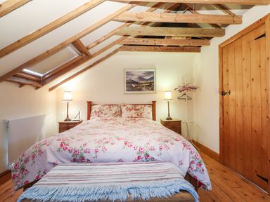 A bedroom with a double bed floral bedding two bedside tables with lamps exposed wooden ceiling beams and a wooden door at Mrs Delaney's Loft in Ardfinnan near Clonmel County Tipperary