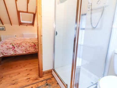 A bathroom with a shower and toilet next to a bedroom with a bed covered in floral bedding at Mrs Delaney's Loft in Ardfinnan near Clonmel County Tipperary