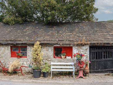 A stone wall with red windows and potted plants at Mrs Delaney's Loft in Ardfinnan near Clonmel, County Tipperary
