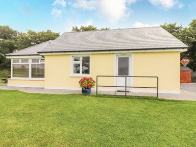 A yellow bungalow with a white door and windows on a lawn at Moybella Lodge in Lisselton near Ballybunion County Kerry