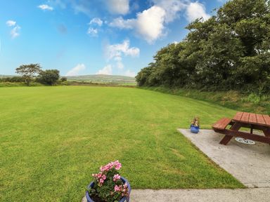A large grassy field with two potted plants and a wooden picnic table on a concrete slab at Moybella Lodge in Lisselton near Ballybunion County Kerry